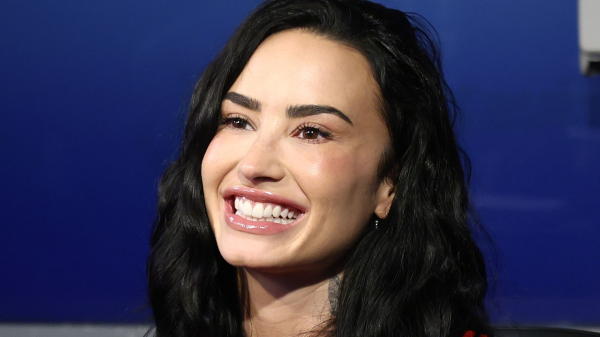 Demi Lovato smiling in a red shirt against a blue background